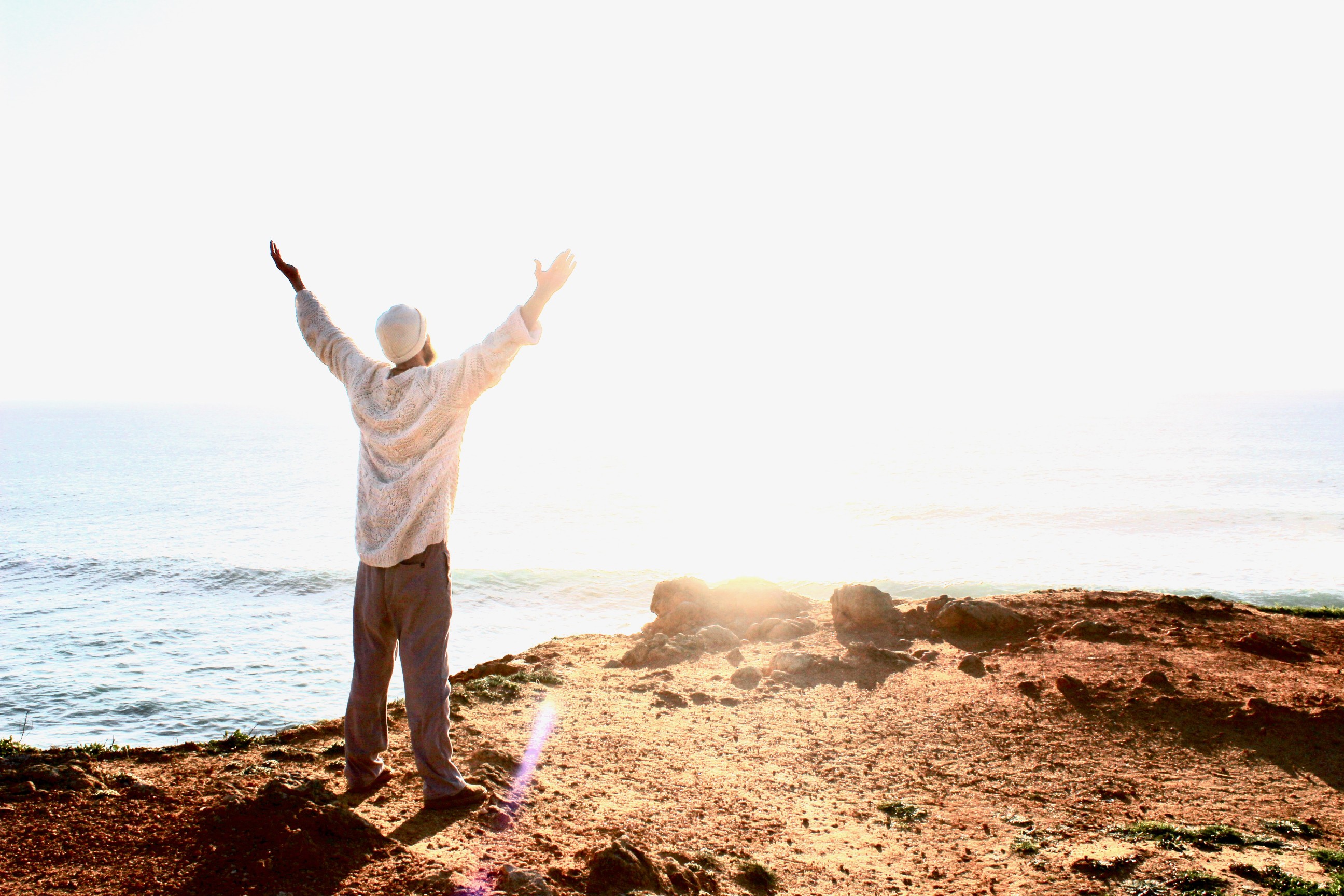 Michaël Bijker standing in victory pose facing the sun on a cliff